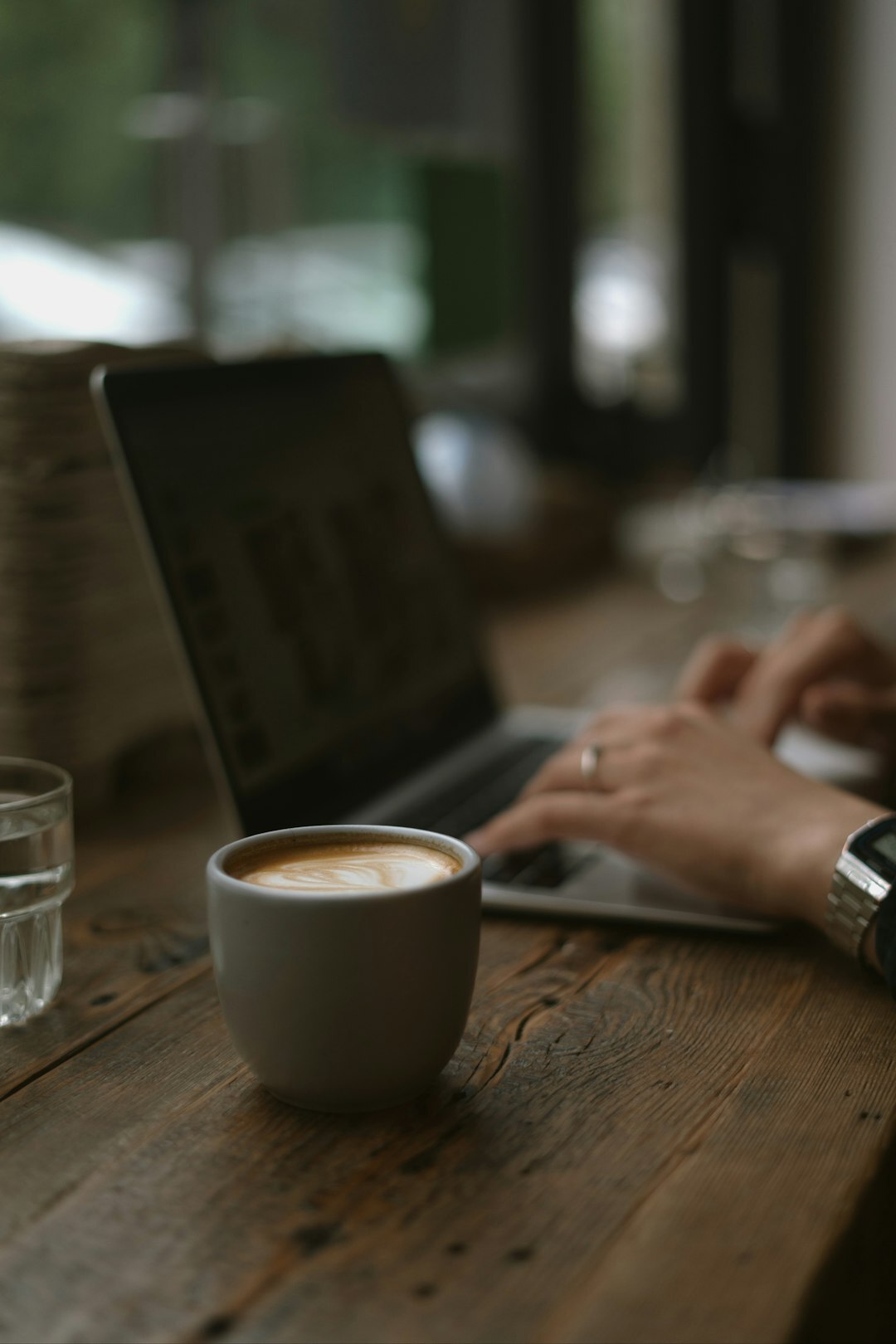 Close up of hands typing on a laptop with a coffee cup nearby